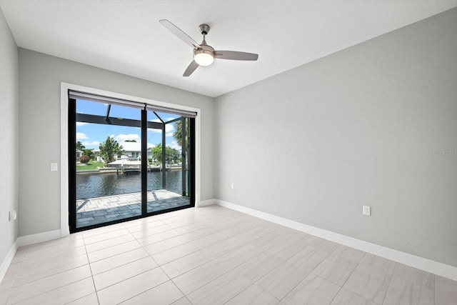 tiled empty room featuring ceiling fan and a water view