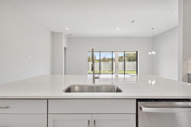 kitchen with white cabinets, stainless steel dishwasher, hanging light fixtures, and light stone counters