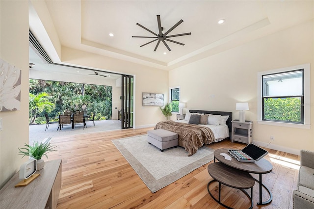 bedroom with a raised ceiling, access to outside, and light wood-type flooring