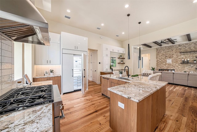 kitchen with stainless steel gas range oven, white cabinetry, decorative light fixtures, a center island with sink, and island exhaust hood