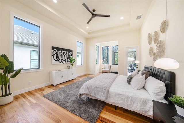 bedroom featuring ceiling fan, multiple windows, a tray ceiling, and light hardwood / wood-style flooring