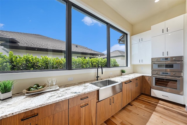 kitchen featuring sink, light stone countertops, light hardwood / wood-style floors, white cabinets, and stainless steel double oven