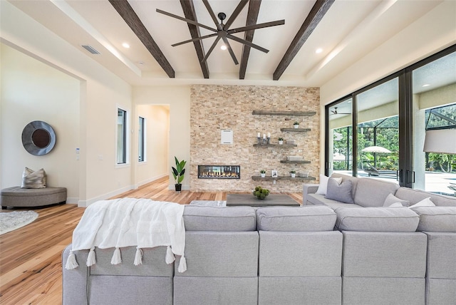 living room with beam ceiling, light hardwood / wood-style floors, a large fireplace, and ceiling fan