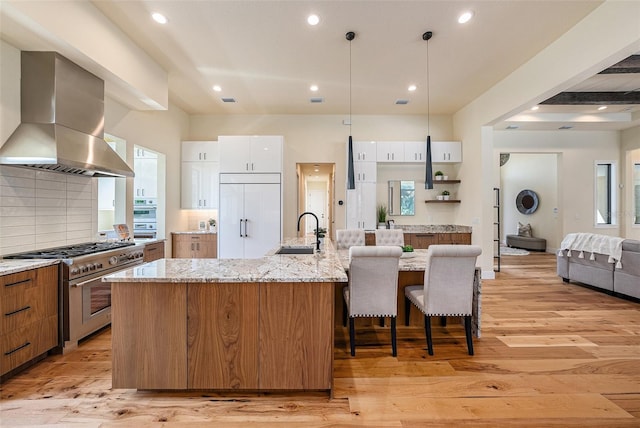 kitchen featuring island range hood, white cabinetry, sink, high end appliances, and a kitchen island with sink