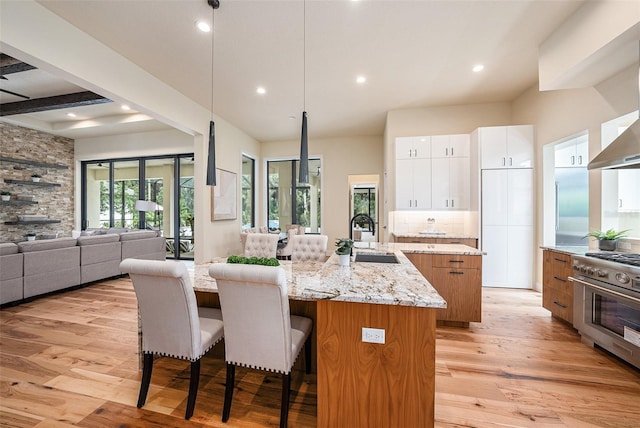 kitchen with high end stainless steel range, white cabinetry, an island with sink, light stone countertops, and light hardwood / wood-style floors