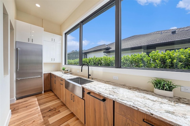 kitchen featuring light stone counters, stainless steel built in fridge, sink, and white cabinets