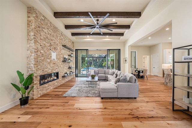 living room featuring beamed ceiling, a stone fireplace, a towering ceiling, and light hardwood / wood-style flooring