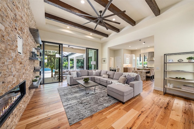 living room featuring ceiling fan, beam ceiling, a towering ceiling, a fireplace, and light hardwood / wood-style floors