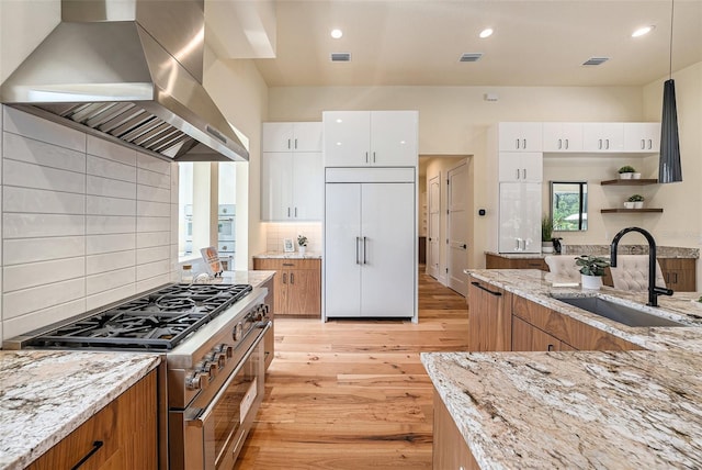 kitchen featuring high quality appliances, white cabinetry, sink, exhaust hood, and light stone counters