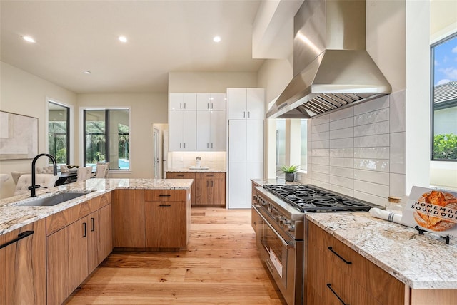 kitchen with sink, white cabinetry, light stone counters, high end range, and island exhaust hood