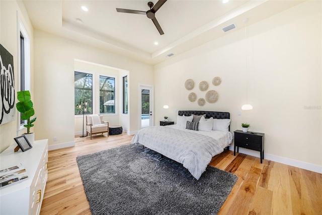 bedroom featuring ceiling fan, light wood-type flooring, and a tray ceiling