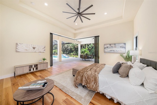 bedroom featuring a towering ceiling, wood-type flooring, access to exterior, ceiling fan, and a tray ceiling