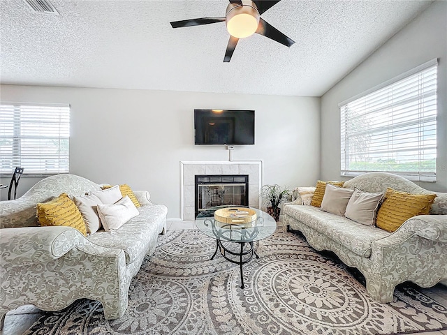 living room with a textured ceiling, ceiling fan, and a tiled fireplace