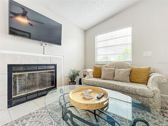 living room with a textured ceiling, a tiled fireplace, lofted ceiling, light tile patterned floors, and ceiling fan