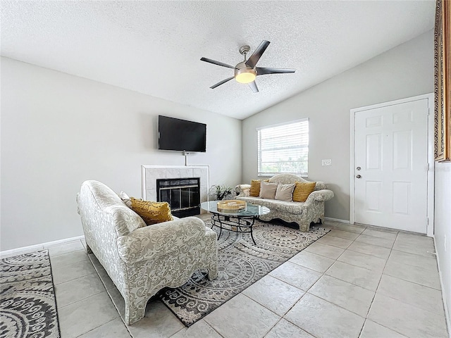 living room with light tile patterned floors, a tile fireplace, vaulted ceiling, a textured ceiling, and ceiling fan