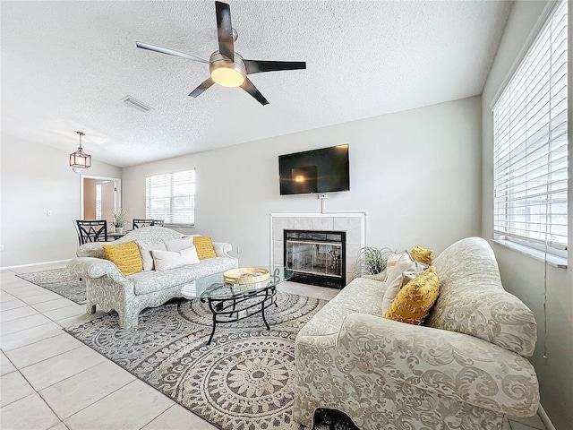 tiled living room with ceiling fan, a textured ceiling, and a tile fireplace