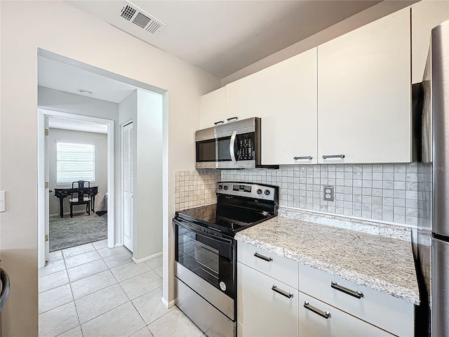 kitchen featuring appliances with stainless steel finishes, backsplash, white cabinetry, light stone counters, and light tile patterned floors