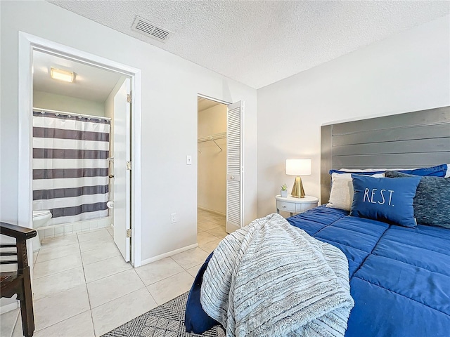 bedroom with a closet, a spacious closet, connected bathroom, a textured ceiling, and light tile patterned floors