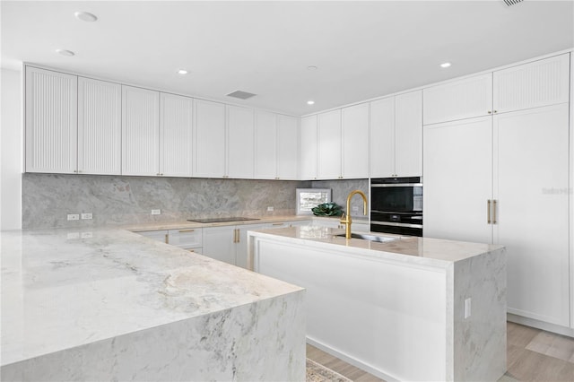 kitchen with a kitchen island with sink, white cabinetry, black appliances, sink, and decorative backsplash