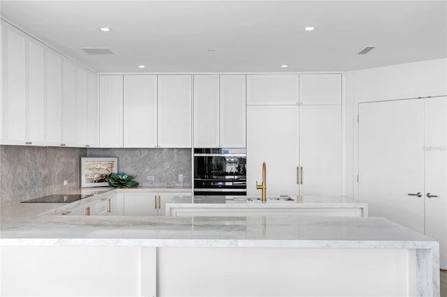 kitchen featuring black electric stovetop, backsplash, sink, light stone countertops, and white cabinets