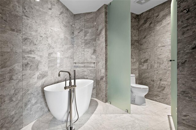 bathroom featuring a tub to relax in, tile walls, and toilet