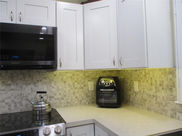 kitchen featuring decorative backsplash, white cabinetry, and stove