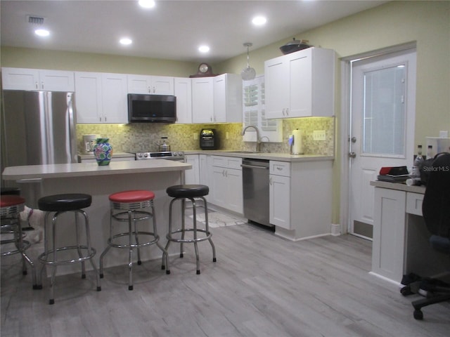 kitchen featuring stainless steel appliances, decorative backsplash, sink, light wood-type flooring, and a breakfast bar area