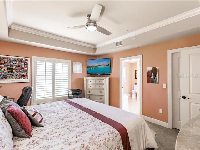 carpeted bedroom featuring crown molding, a tray ceiling, ensuite bathroom, and ceiling fan