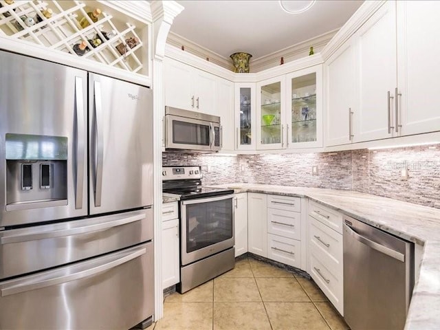 kitchen featuring white cabinets, appliances with stainless steel finishes, light stone counters, light tile patterned flooring, and tasteful backsplash