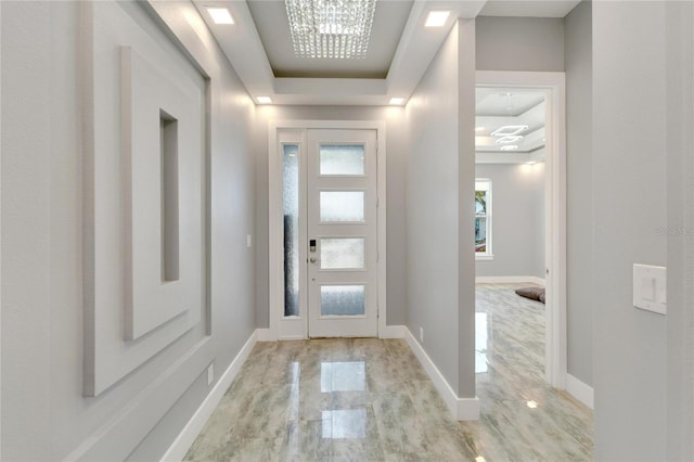 entryway featuring a tray ceiling, light wood-style floors, and baseboards