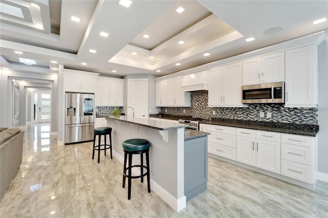 kitchen featuring a center island with sink, a breakfast bar area, a tray ceiling, stainless steel appliances, and white cabinetry