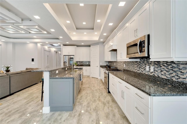 kitchen with a tray ceiling, stainless steel appliances, open floor plan, white cabinetry, and a large island with sink