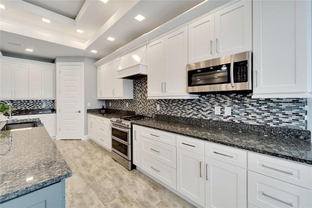 kitchen with appliances with stainless steel finishes, white cabinets, a sink, and premium range hood