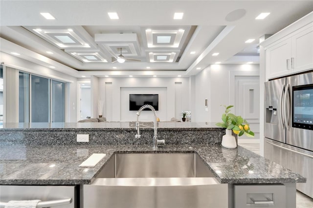 kitchen featuring open floor plan, white cabinetry, a sink, dark stone counters, and stainless steel fridge