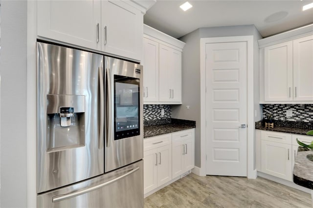 kitchen with decorative backsplash, stainless steel fridge, dark stone countertops, and white cabinetry