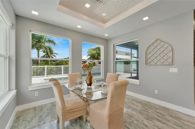 dining room with a raised ceiling, a notable chandelier, light wood-style flooring, and baseboards