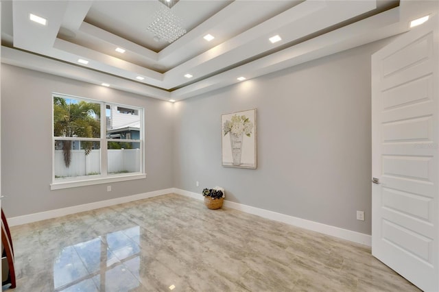 spare room with recessed lighting, a raised ceiling, and baseboards