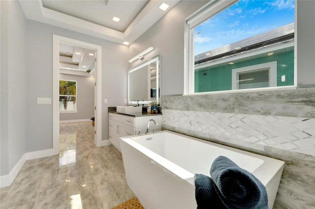 bathroom with a raised ceiling, a freestanding tub, vanity, and baseboards