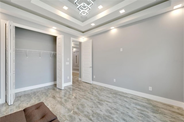 unfurnished bedroom featuring a tray ceiling, a closet, and baseboards