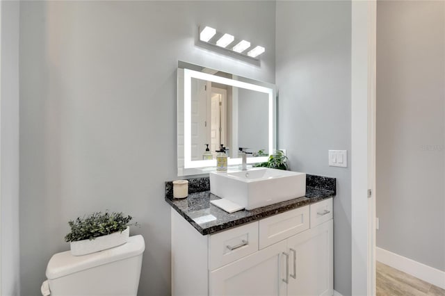 bathroom featuring toilet, baseboards, wood finished floors, and vanity