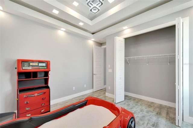 bedroom with light wood-type flooring, a tray ceiling, a closet, and baseboards