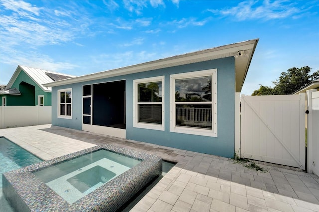 rear view of property featuring a patio area, a fenced backyard, a gate, and an in ground hot tub