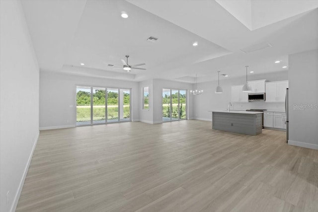 unfurnished living room with a wealth of natural light, a raised ceiling, light wood-style flooring, and baseboards