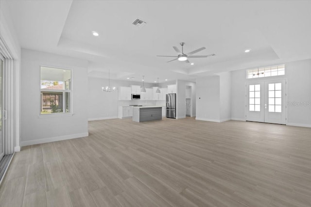 unfurnished living room with light wood-style floors, a raised ceiling, baseboards, and french doors