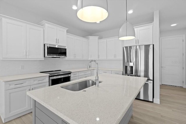 kitchen with a center island with sink, appliances with stainless steel finishes, white cabinetry, pendant lighting, and a sink