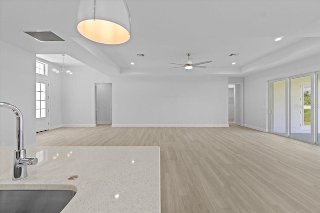 unfurnished living room featuring light wood-type flooring, a raised ceiling, visible vents, and a sink