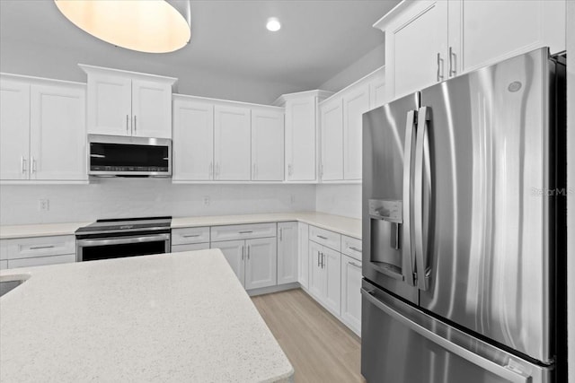 kitchen with recessed lighting, light wood-style flooring, appliances with stainless steel finishes, white cabinetry, and light stone countertops