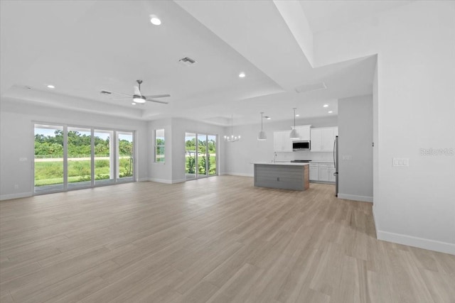 unfurnished living room with light wood-style floors, visible vents, a tray ceiling, and baseboards