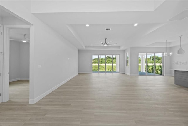 unfurnished living room with ceiling fan with notable chandelier, a raised ceiling, light wood-style flooring, and baseboards