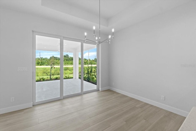 empty room with light wood-type flooring, baseboards, a chandelier, and a raised ceiling